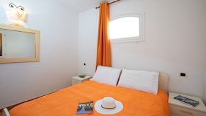 A bedroom with an orange bedspread, a white hat, and a book on the nightstand. - Casa Dello Chef by Wonderful Italy (Santa Teresa di Gallura)
