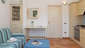 A compact kitchen with a dining area, a sofa, and a small table with a magazine. - Casa Dello Chef by Wonderful Italy (Santa Teresa di Gallura)