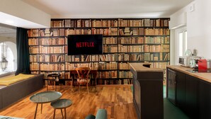 A cozy living room with a bookshelf, a flat-screen TV, a dining area, and a kitchenette. - Turin Bed Books by Wonderful Italy (Turin)