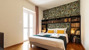 A bedroom with a large bed, a bookshelf, and a window with curtains. - Turin Bed Books by Wonderful Italy (Turin)