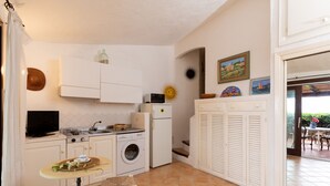 A compact kitchen with white cabinets, a washing machine, a small table with a basket, and a door leading to an outdoor area. - Casa del Bonsai by Wonderful Italy (Arzachena)