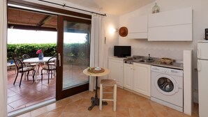 A compact kitchen with a washing machine, a dining area with chairs, and a table with a vase. - Casa del Bonsai by Wonderful Italy (Arzachena)
