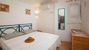 A bedroom with a bed, a headboard, a bedside table with a magazine, a wall-mounted air conditioner, and a mirror with a teal frame. - Casa del Bonsai by Wonderful Italy (Arzachena)