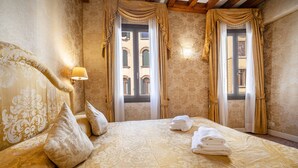 A hotel room with a large bed, two windows with curtains, a wall-mounted lamp, and a view of a building through the windows. - Ca di Malta Room 1 by Wonderful Italy (Venice)