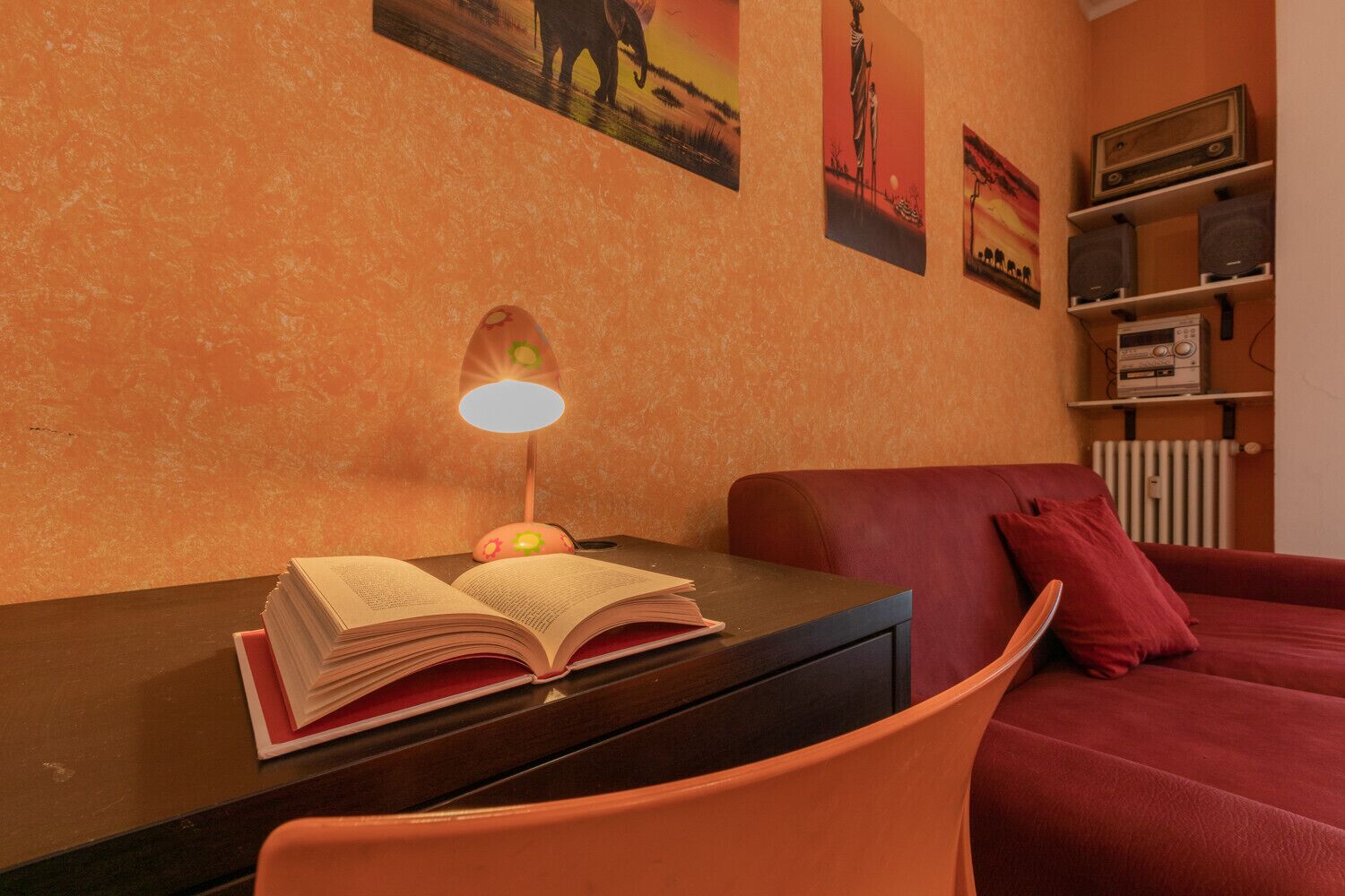 A room with a bed, a desk with an open book, a lamp, and a radiator.