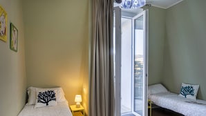 Una habitación con dos camas, una ventana con cortinas y una mesita de noche con lámpara.
