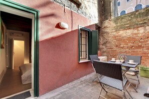Un'accogliente area esterna con sedie in vimini e un tavolo, una porta che dà su una stanza, e un muro in mattoni.