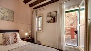 A bedroom with a large bed, a nightstand, a window with curtains, and a view of an outdoor brick wall. - I Quattro Mori by Wonderful Italy (Venice)