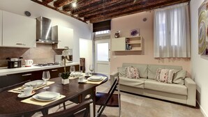A modern kitchen with a wooden ceiling, a dining area with a table set for four, and a living room with a sofa and a window with curtains. - I Quattro Mori by Wonderful Italy (Venice)
