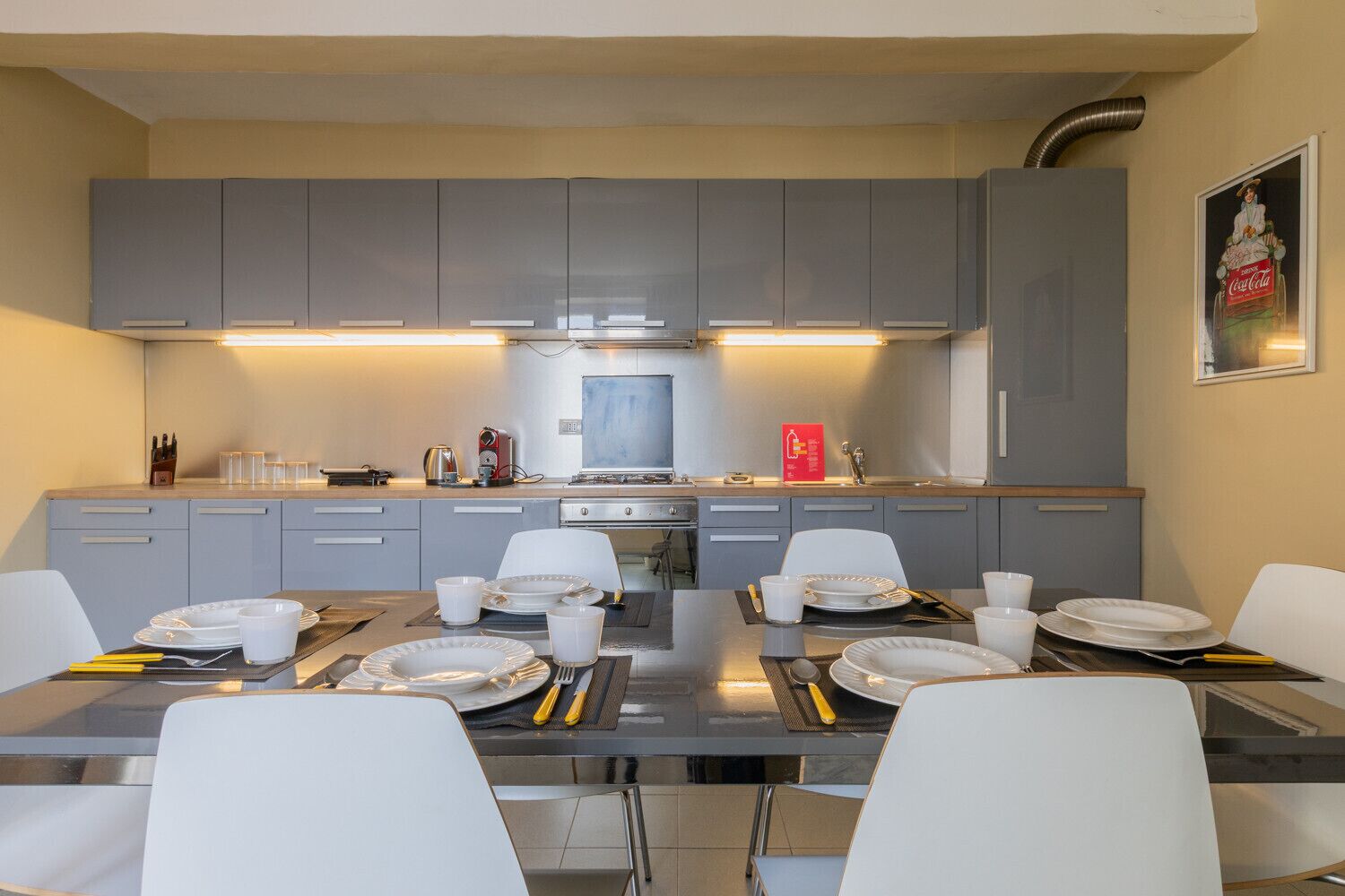 A modern kitchen with grey cabinets, a stainless steel range, and a dining area with white chairs and plates.