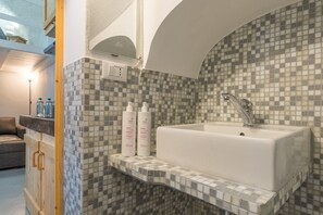 Un baño con un revestimiento de mosaico en la pared, un lavamanos blanco y dos botellas de champú en una estantería.
