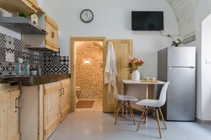 Una cocina con armarios de madera, salpicadero de azulejos, refrigerador de acero inoxidable, una mesa de comedor con sillas y un reloj en la pared.