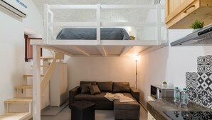 Un espace de vie compact comprenant un lit superposé, un canapé, une petite table et un coin cuisine.
