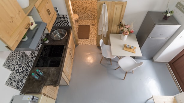 Une cuisine de taille réduite, équipée d’un évier, d’une cuisinière et de chaises blanches.