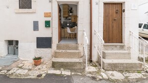 Un bâtiment avec une porte en bois, un petit porche avec des marches et un pot de fleurs.