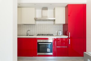 Una cocina con armarios rojos, una campana extractora de acero inoxidable, una estufa a gas, un horno y una cafetera.