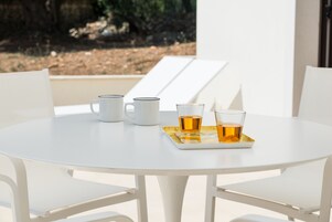 Una mesa redonda blanca con cuatro tazas blancas y dos vasos de líquido ámbar, probablemente té, sobre una bandeja.