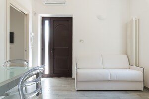 Una sala de estar moderna con una mesa de comedor de vidrio, un sofá blanco y una puerta marrón.