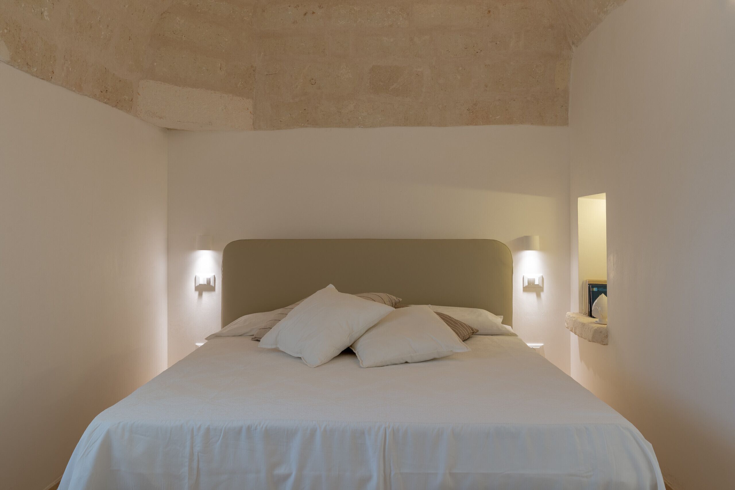 A bedroom with a large bed, two wall-mounted lights, and a stone ceiling.