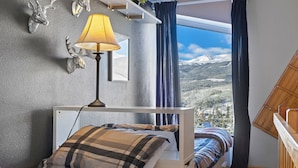 Una camera da letto con un letto a castello, una lampada, vista su un paesaggio innevato e un soffitto in legno.