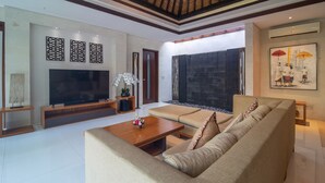 A modern living room with a large flat-screen TV, a sofa, a coffee table, and decorative elements like wall art and an orchid plant. - Rekso Villa·Seaside Serenity,Elegant Escape, Beach (Unit 2009)