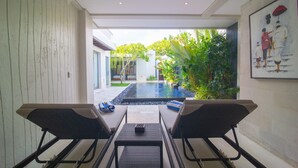A modern pool area with lounge chairs and a small table, surrounded by greenery and a view of a building. - Rekso Villa·Seaside Serenity,Elegant Escape, Beach (Unit 2009)