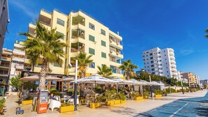A coastal hotel with outdoor seating, palm trees, and a clear blue sky. - The Ultimate Jacuzzi Penthouse by PS (Durrës)
