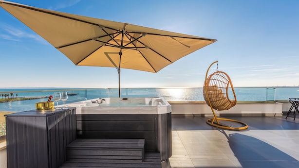 A rooftop terrace with a hot tub, a cushioned seating area, a hanging chair, and a large umbrella providing shade. - The Ultimate Jacuzzi Penthouse by PS (Durrës)