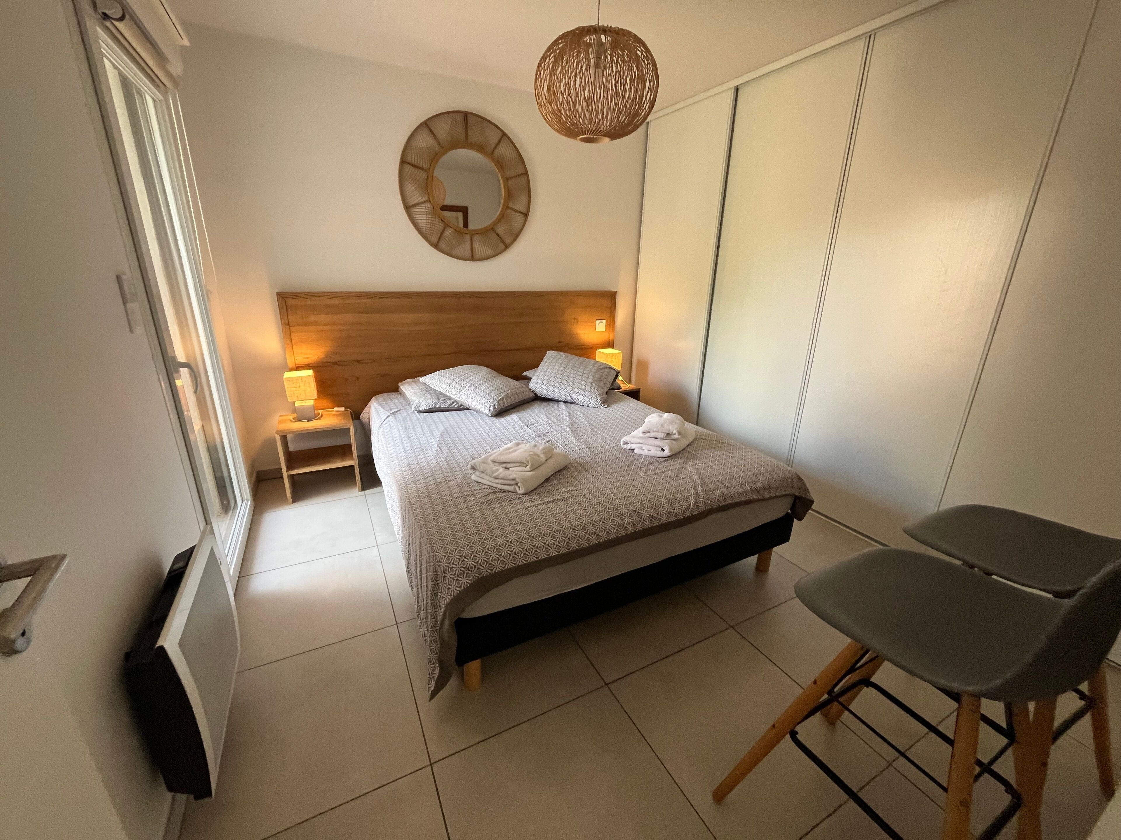 A neatly arranged bedroom with a bed, bedside lamps, a chair, and a wall-mounted mirror.