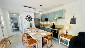 A modern kitchen with a dining area, featuring a wooden table set for four, a black sofa, and a small side table with a lamp. - V0755-Villa sleeps 6 in residence with communal pool close to the sea (Vias)