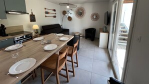 A modern kitchen with a dining area, featuring a wooden table set for four, a black sofa, and a TV mounted on the wall. - V0755-Villa sleeps 6 in residence with communal pool close to the sea (Vias)