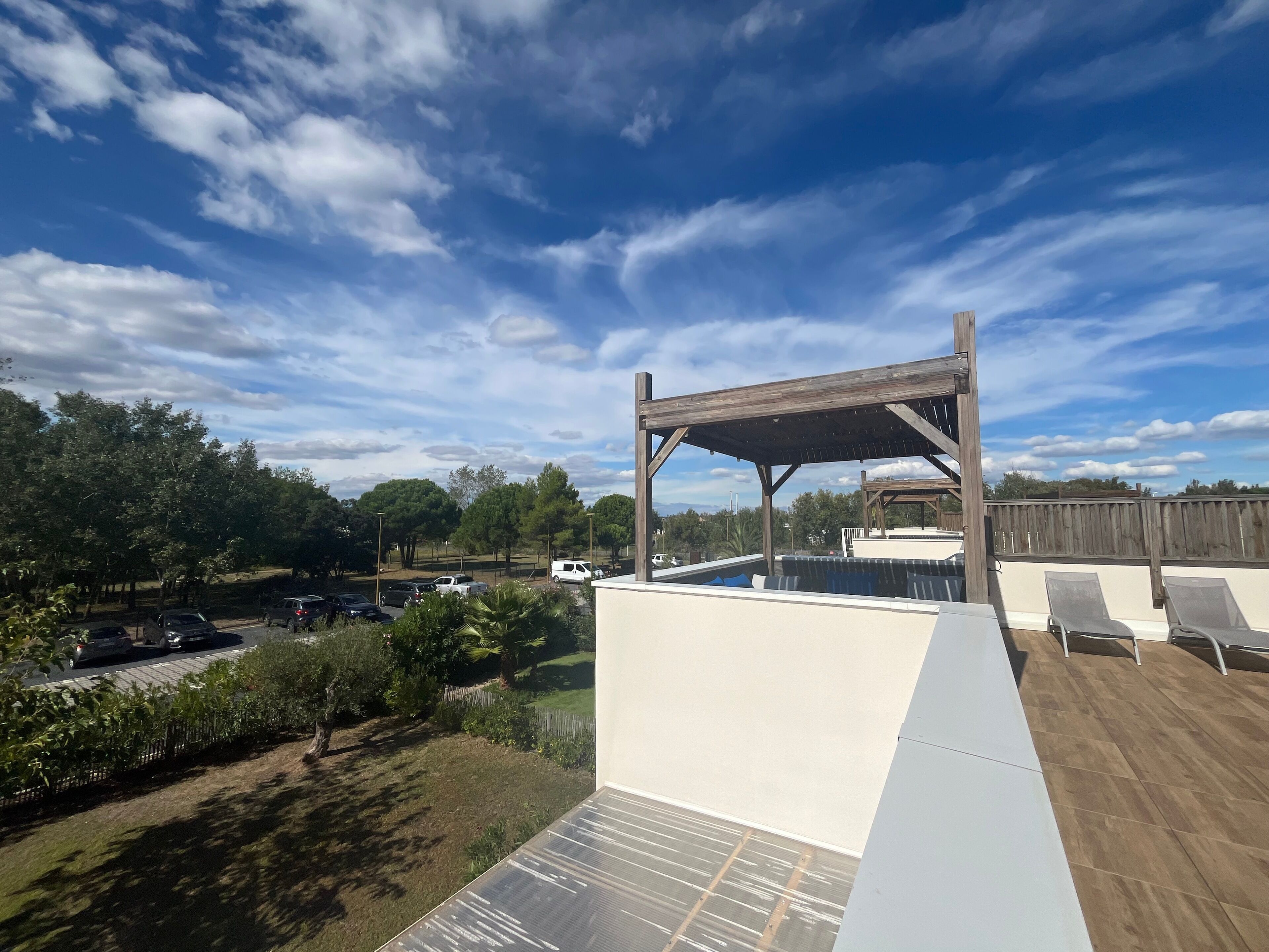 Une terrasse sur le toit agrémentée d’une pergola en bois, une piscine et une vue sur un parking.