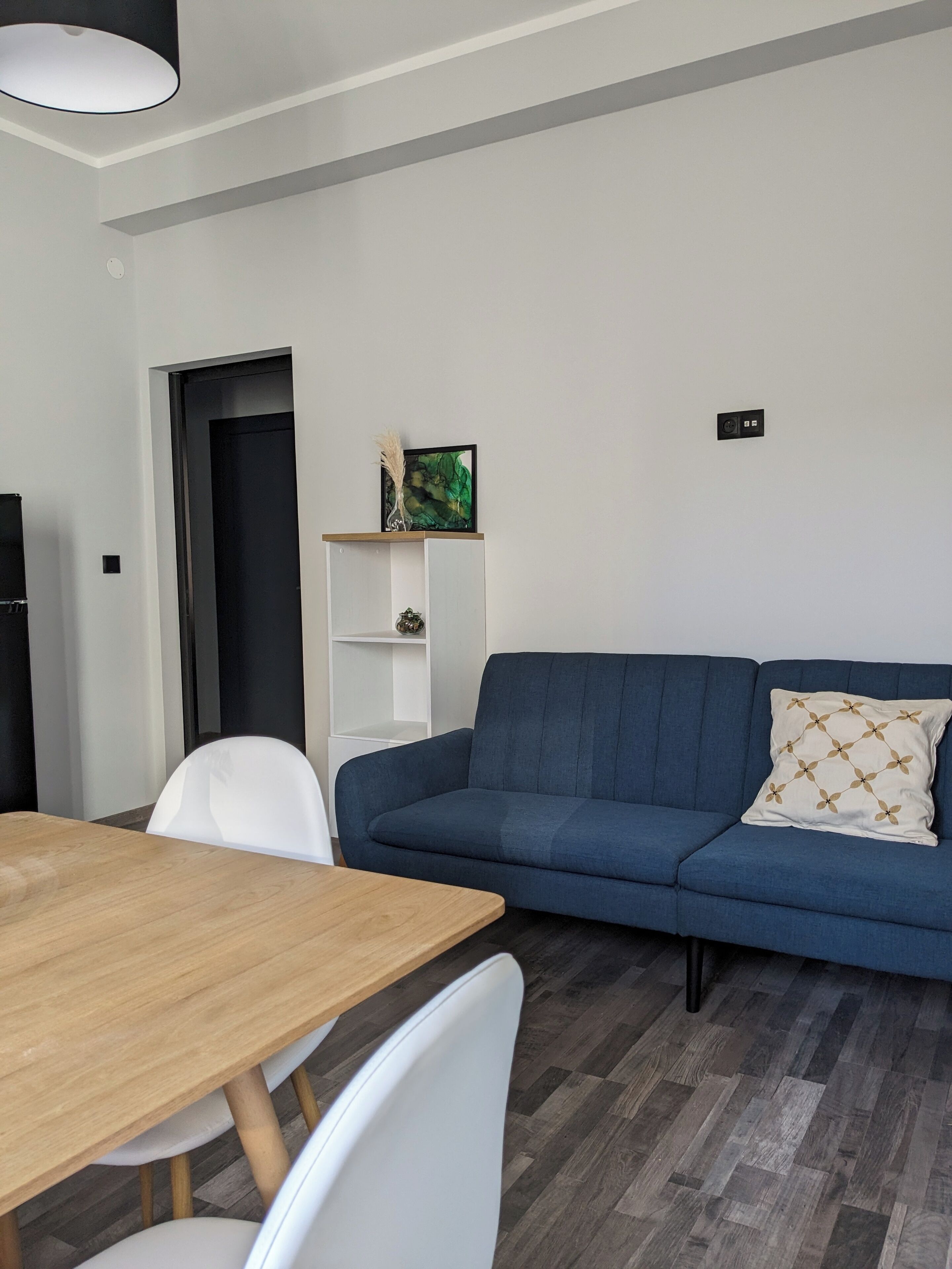 Un soggiorno moderno con un divano blu, un tavolo da pranzo in legno, sedie bianche e una scaffalatura bianca su una parete bianca.