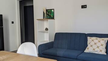 Un soggiorno moderno con un divano blu, un tavolo da pranzo in legno, sedie bianche e una scaffalatura bianca su una parete bianca.