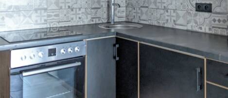 A kitchen with wooden cabinets, a stainless steel oven, a sink, and patterned backsplash tiles.