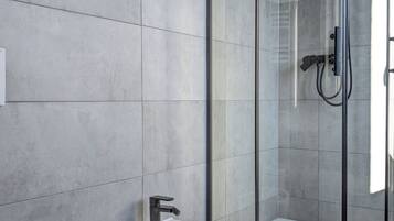 Un baño moderno con un lavamanos independiente, ducha con mampara de vidrio y un inodoro.