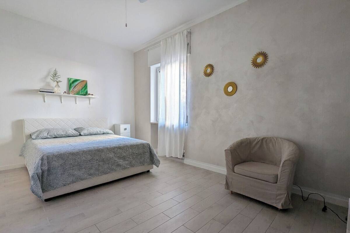 Un dormitorio con cama, una silla, un ventanal con cortinas y adornos en la pared.