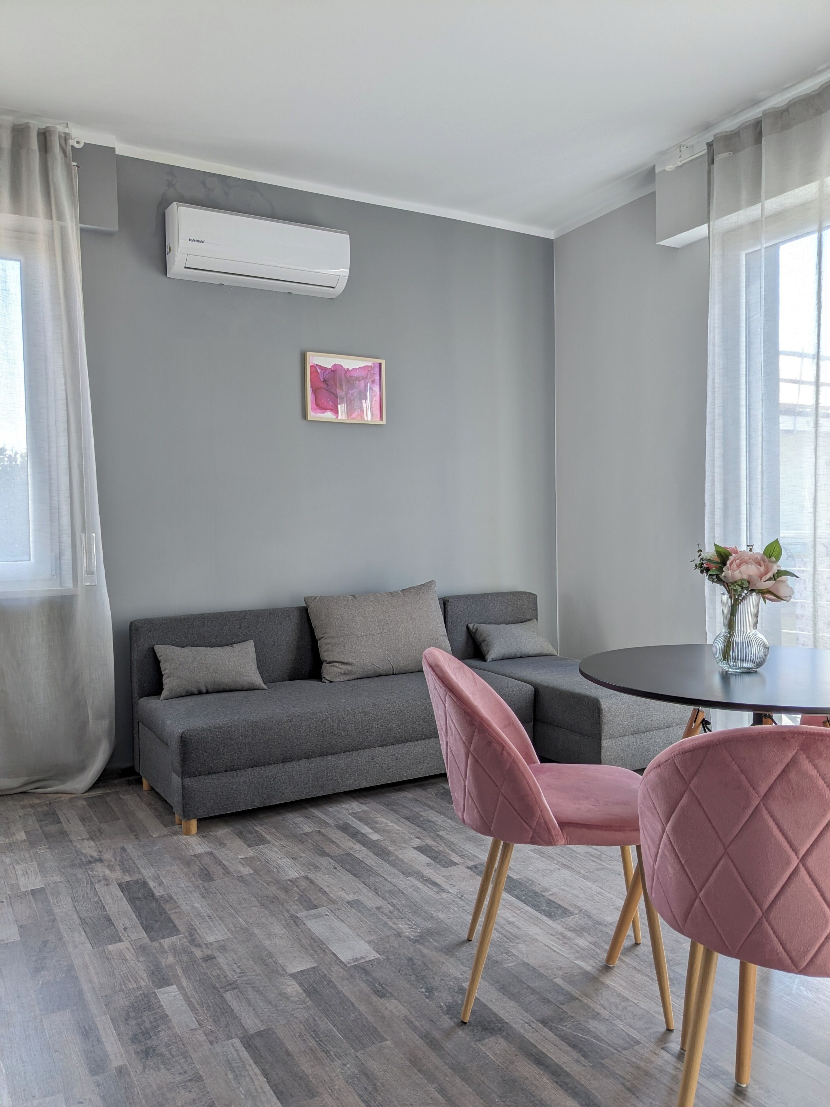 A modern living room with a grey sofa, a pink chair, a small table, and a wall-mounted air conditioner.