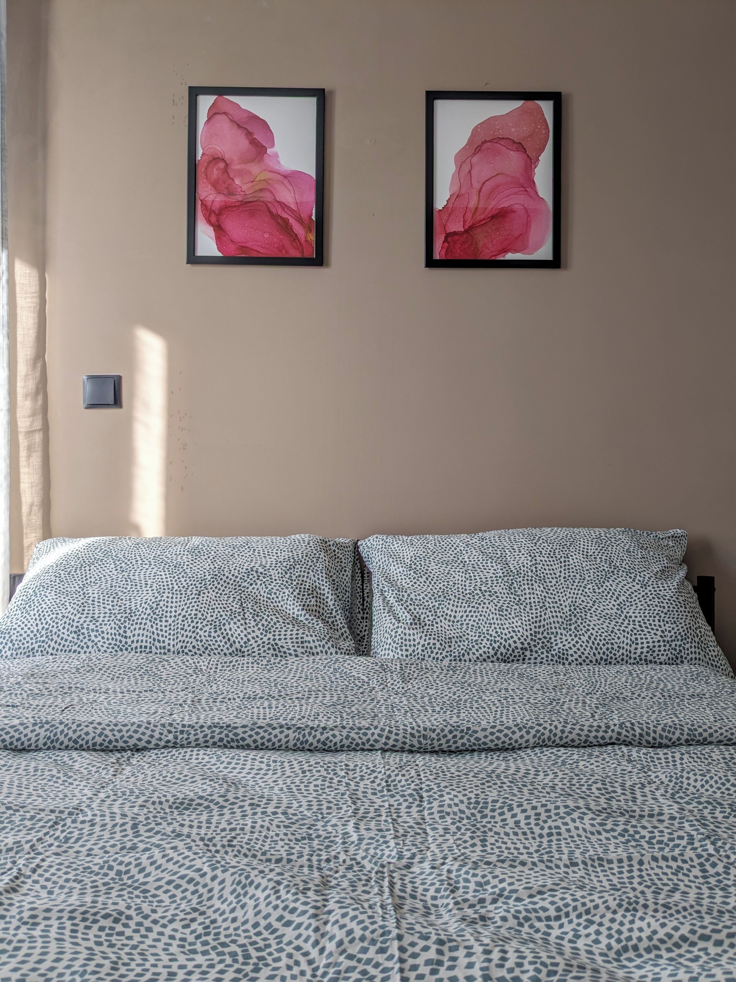 A bedroom with a bed, two framed pictures on the wall, and a light switch.