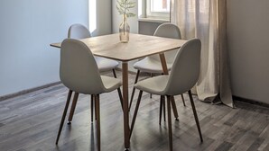Un coin repas avec une table en bois et quatre chaises, un vase avec une plante et une fenêtre avec des rideaux.