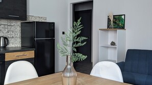 Une cuisine moderne avec un réfrigérateur noir, une table à manger en bois surmontée d’un vase transparent, et un canapé bleu dans l’espace salon.