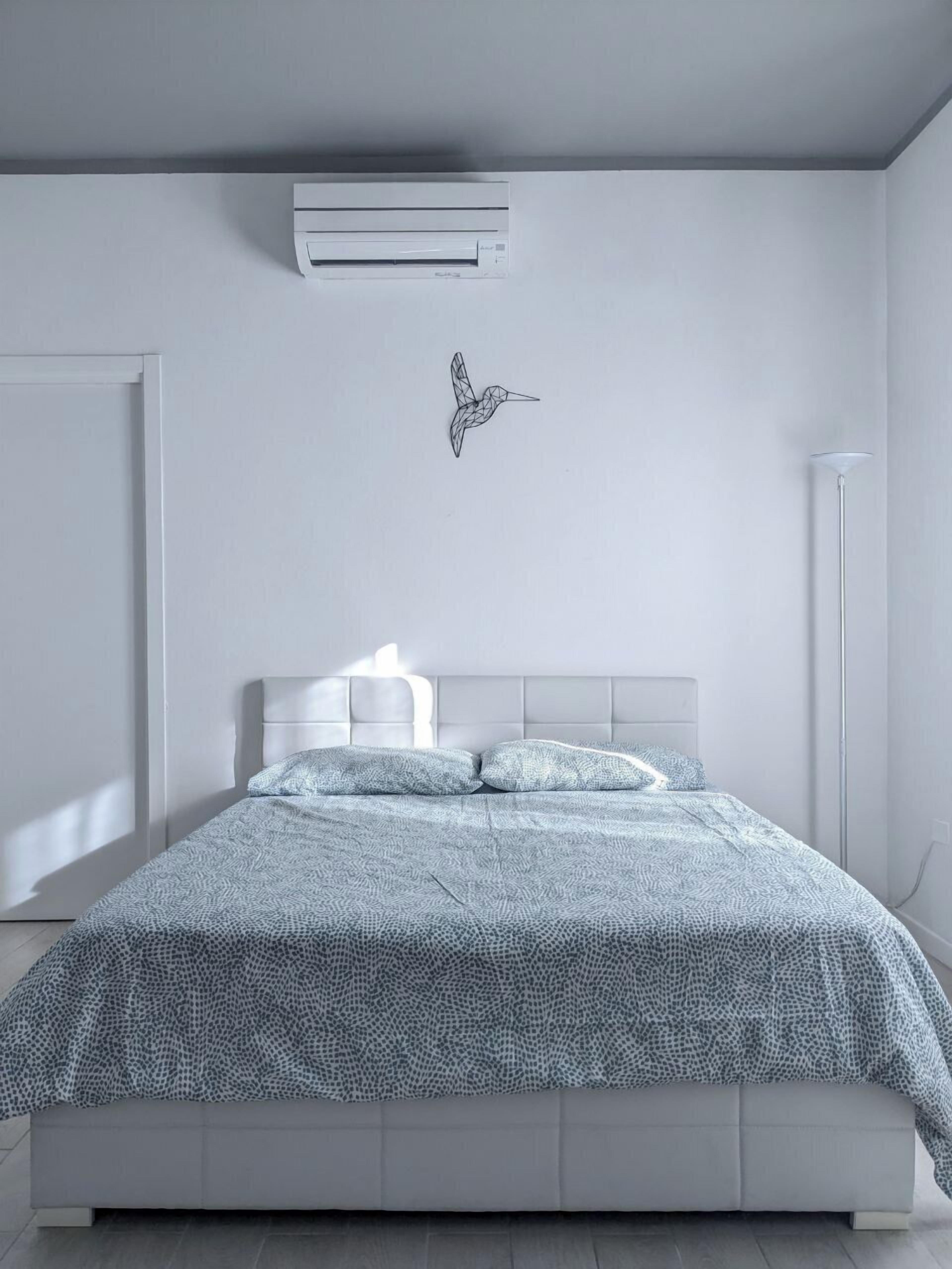 Une chambre moderne avec un lit, une tête de lit blanche et un climatiseur fixé au mur.