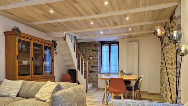 Una sala de estar acogedora con un sofá, una mesa de comedor con sillas, una escalera y un techo de madera.