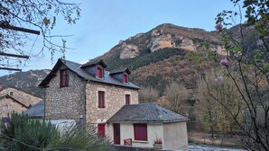 Un edificio de piedra con contraventanas rojas y una pequeña construcción adosada.