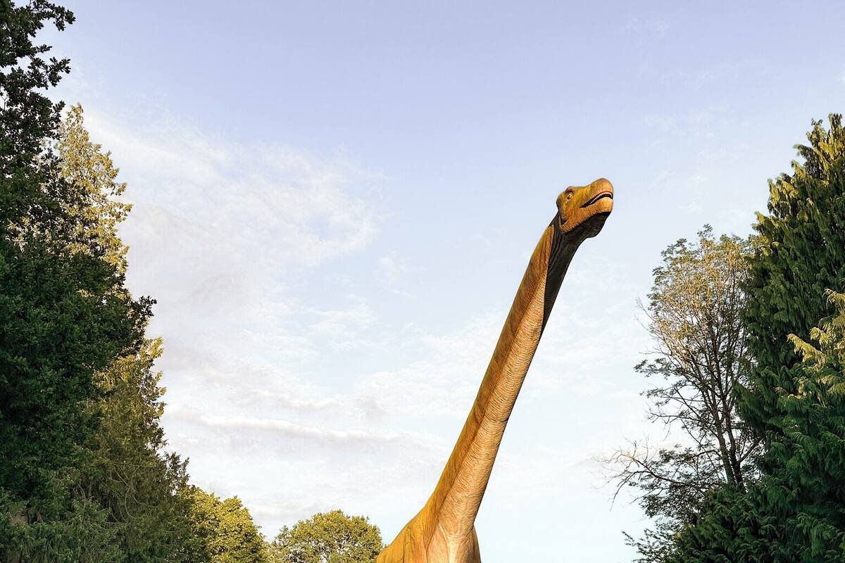 A large dinosaur statue in a natural setting with a dirt path and greenery.