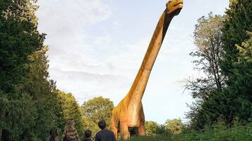 Una estatua grande de dinosaurio en un entorno natural, con un sendero de tierra y vegetación.