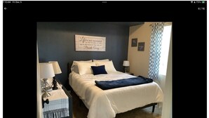 A neatly made bed with a white and blue color scheme, a bedside table with a lamp, and a wall with a motivational quote. - EAA 2026  3-bedroom lake house on lake poygan (Winneconne)