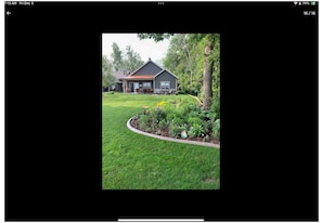 A house with a red roof, surrounded by a well-maintained lawn and a garden with various plants and flowers. - EAA 2026  3-bedroom lake house on lake poygan (Winneconne)