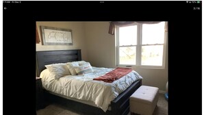 A bedroom with a bed, a nightstand, a window with curtains, and a wall with a framed quote. - EAA 2026  3-bedroom lake house on lake poygan (Winneconne)