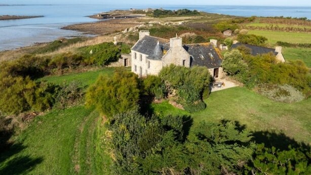 Ein Küstenhaus mit Steinfassade, umgeben von Grün und Blick auf das Meer.